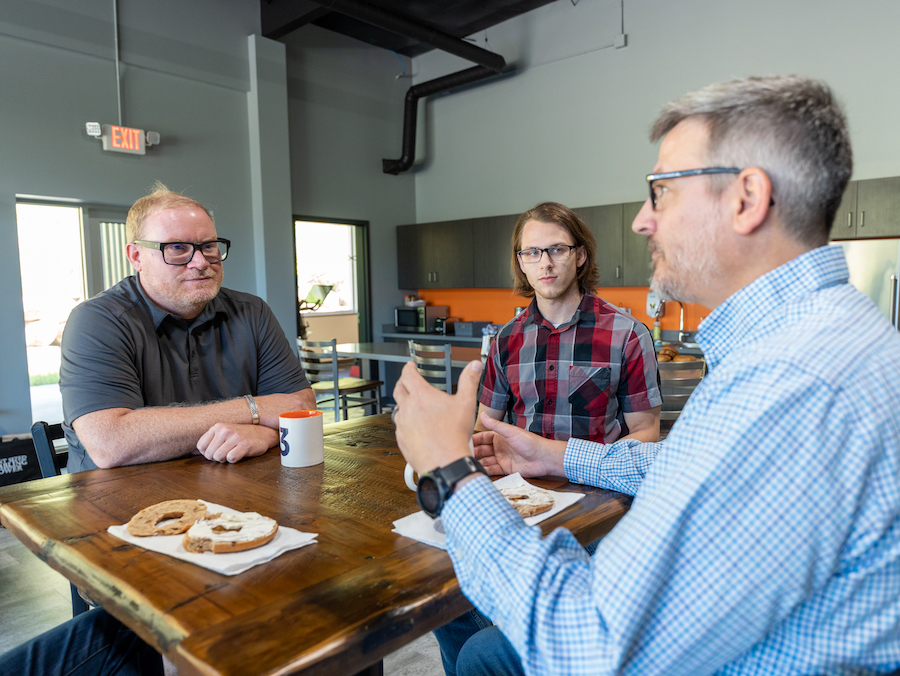 Three i3 team members talking over coffee at a table in the office