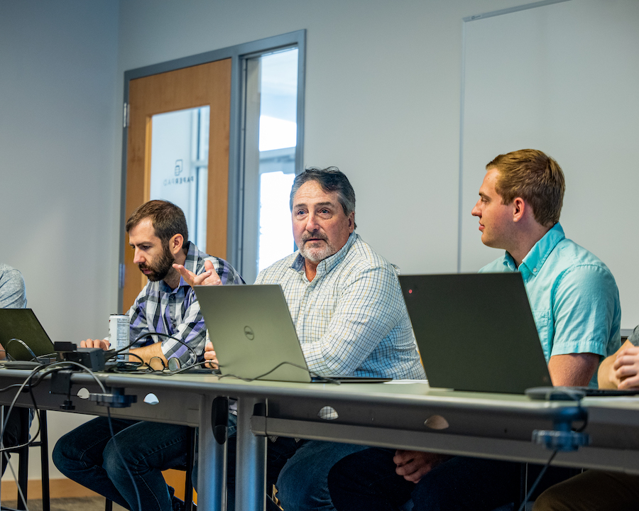 Three engineers working on laptops at a long table during a work session