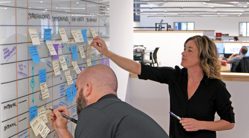 Woman and man looking at whiteboard filled with sticky notes