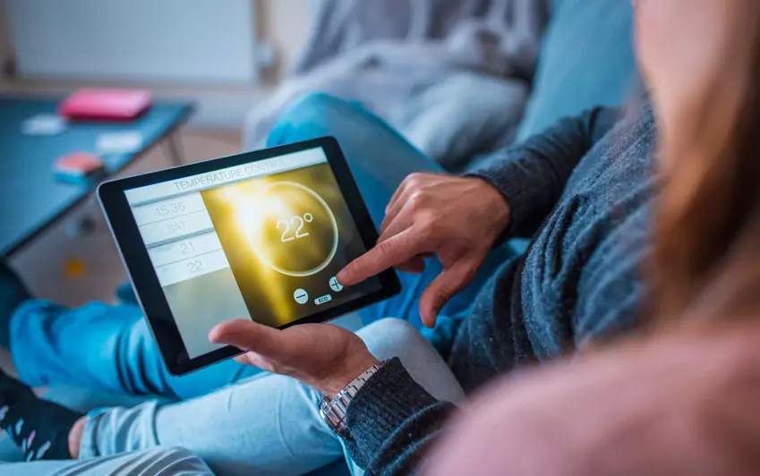 Hands holding a tablet using it to set the temperature of a room