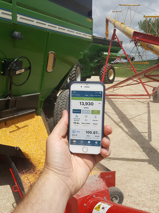 Person holding mobile phone with REAP app tracking the weight coming out of a grain cart