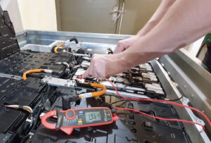 Hands using a voltmeter to repair an electric car battery