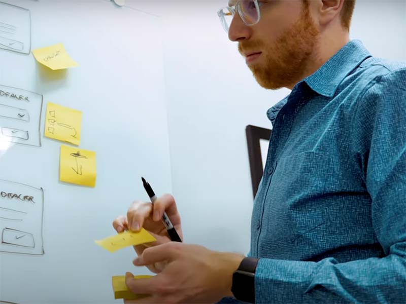 Low angle shot of designer putting sticky notes on a whiteboard.