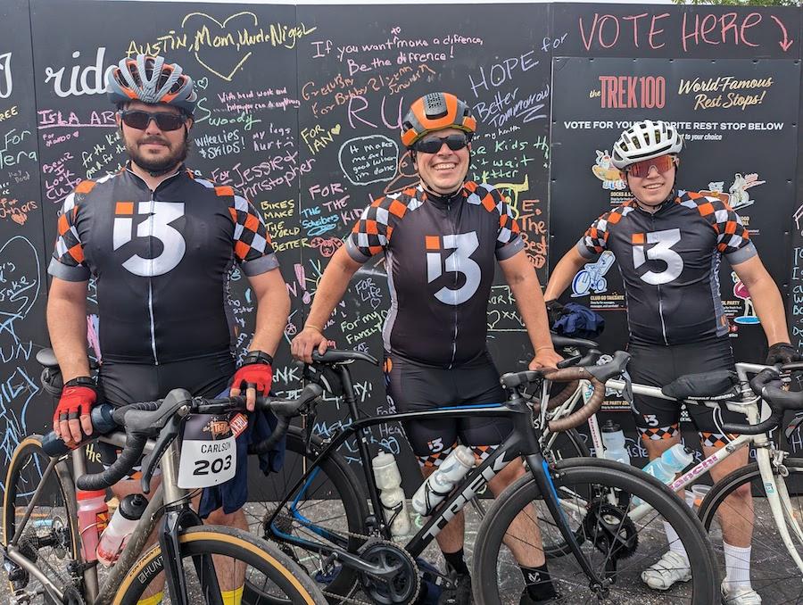 Three cyclists in i3 team jerseys posing with their bikes at a charity ride